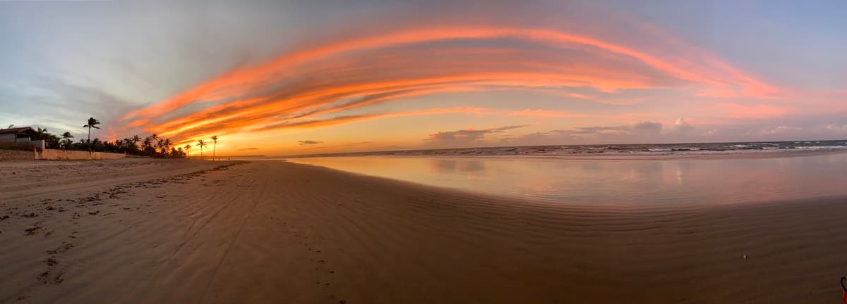 Pôr do sol na praia de Guajiru, com nuvens coloridas e coqueiros na orla